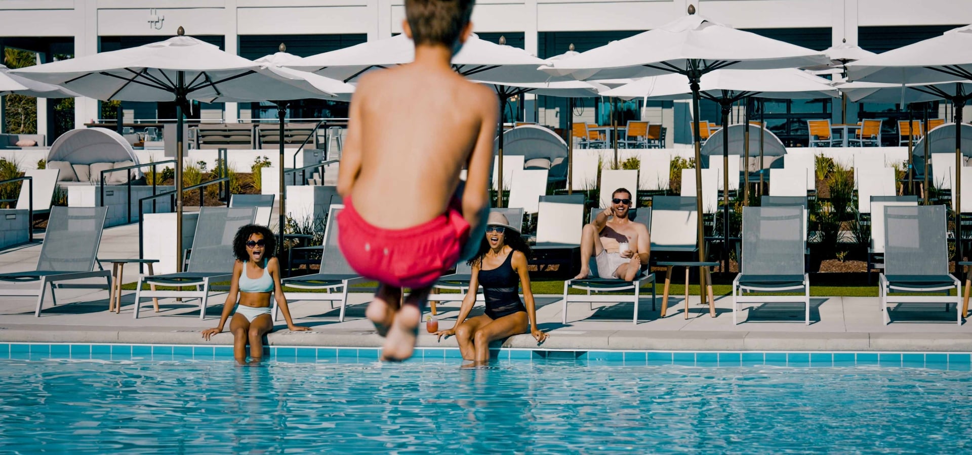 A boy doing a cannon ball into the pool while his family watches