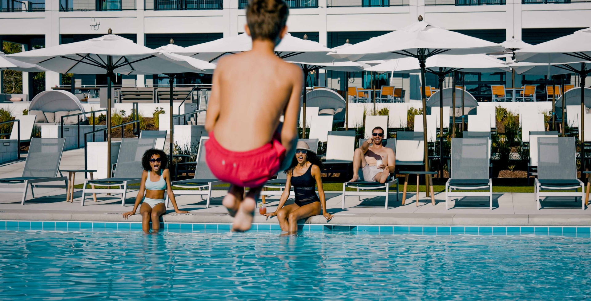 A boy doing a cannon ball into the pool while his family watches