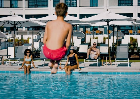 A boy doing a cannon ball into the pool while his family watches
