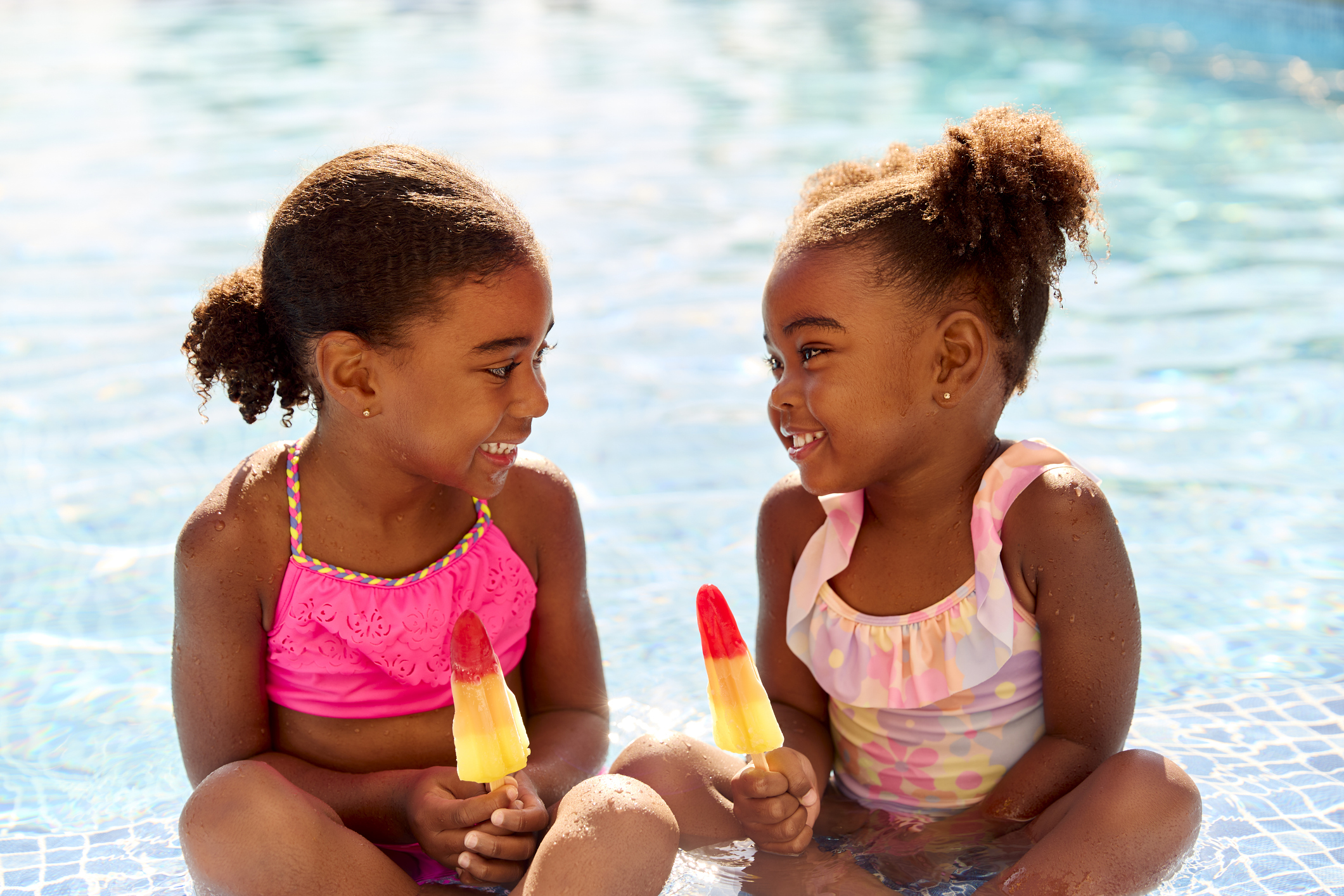Two Girls Eating Ice Lollies in the Swimming Pool