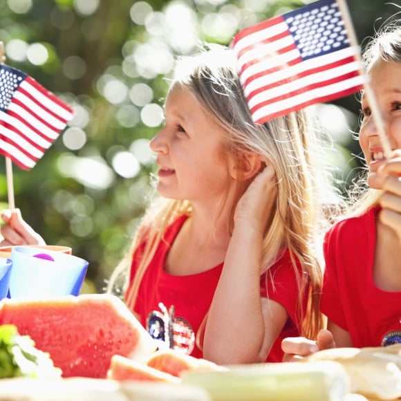 Two girls holding up American Flags smiling surrounded by watermelon