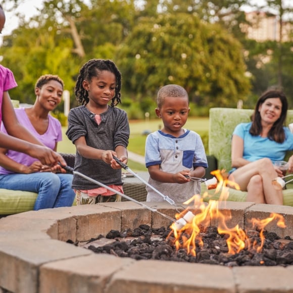 Families sitting around a firepit while the kids are roasting marshmallows
