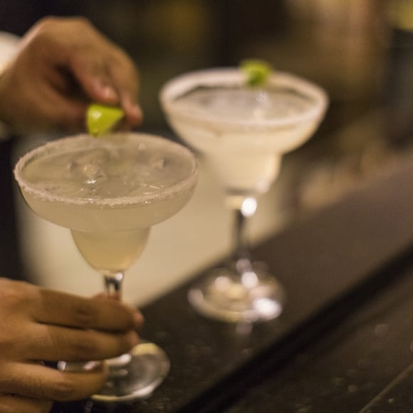 Close-up of an unrecognizable Panamanian bartender putting the final touch on a margarita cocktail by placing a lime wedge on the glass rim.