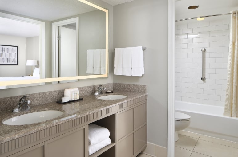 Two section hotel bathroom with a bathtub and double sink