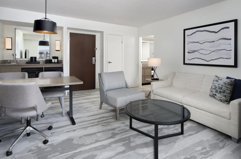 Living room of a suite at the Embassy Suites Myrtle Beach. Couch, chair and circular living room table to the right, and a mini bar to the left with a desk space in front of it.
