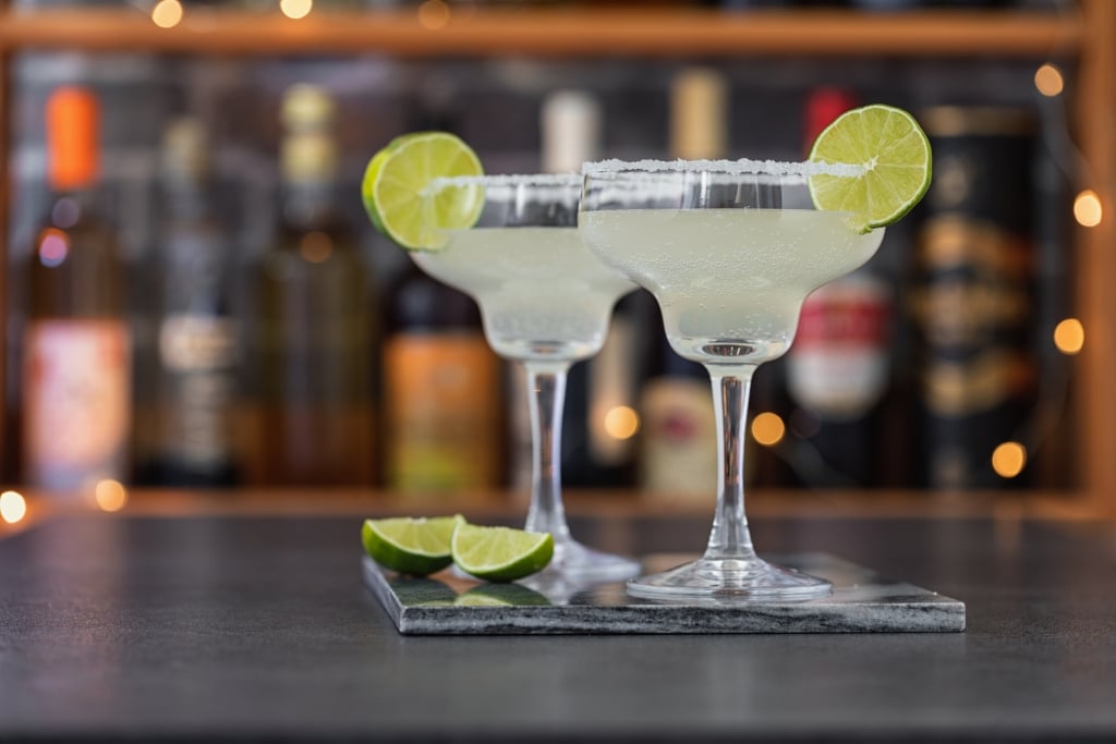 Two glasses of margarita cocktail with a lime on the side