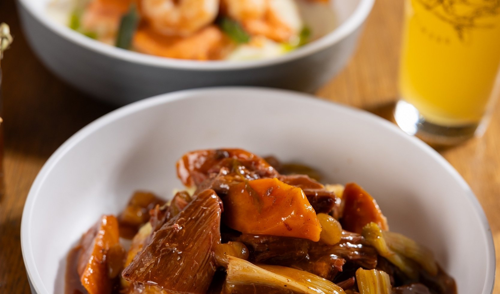 2 bowls of food and a beer on the table. One bowl has Pot Roast and the other has ravioli with shrimp