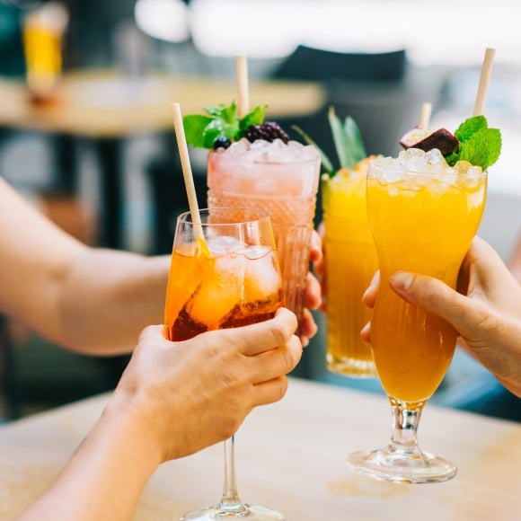 Group of young friends clinking glasses with cocktails in hand celebrating in the afternoon on the terrace