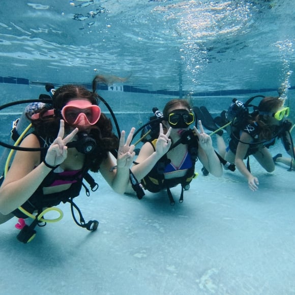 Four scuba divers doing a peace sign under water