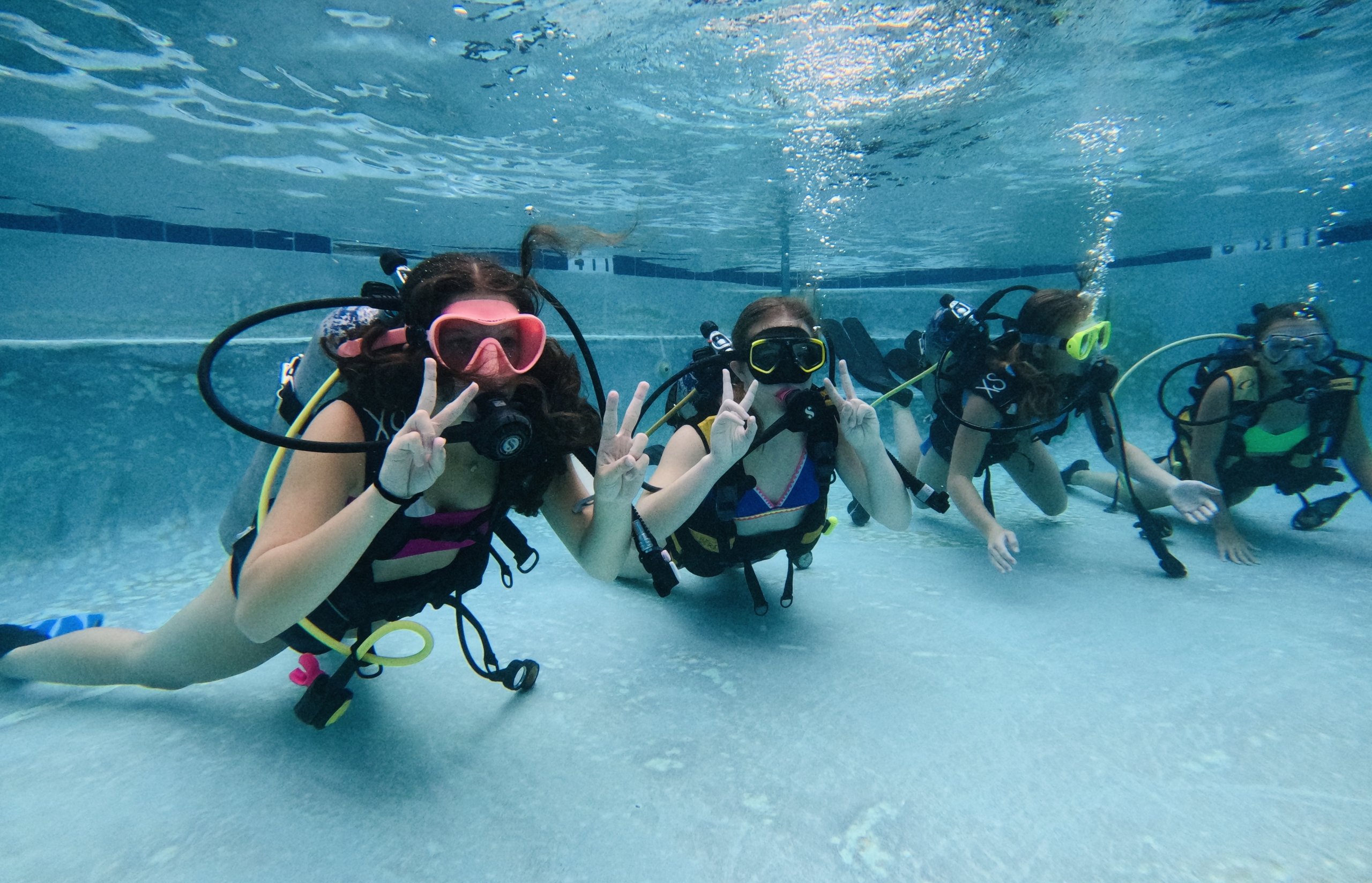 Four scuba divers doing a peace sign under water