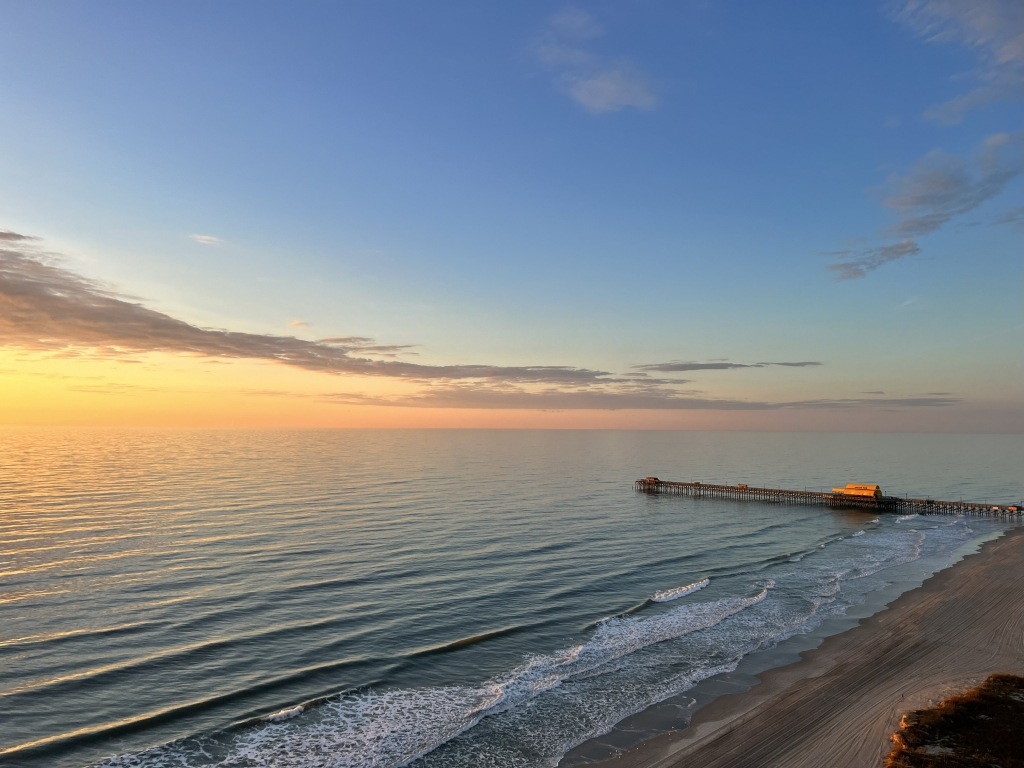 Sunset over a calm sea with an orange horizon and a pier extending into the water on the right side.