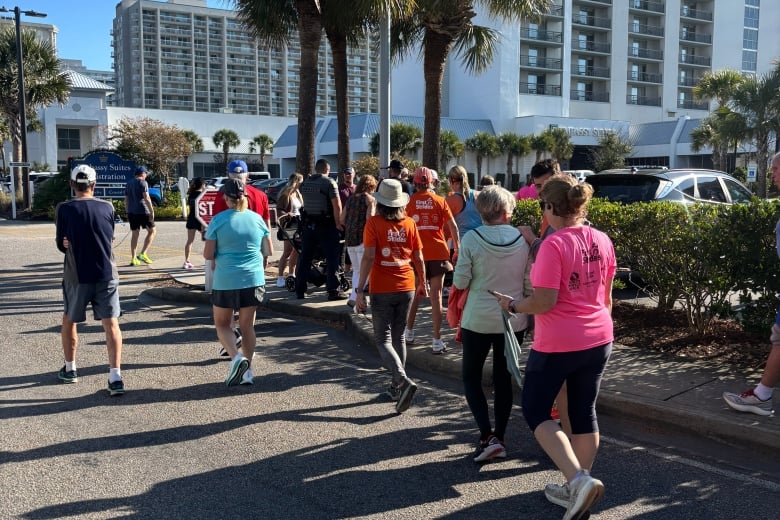 Group of runners and walkers in bright shirts on a sunny hotel street, part of an outdoor charity run.